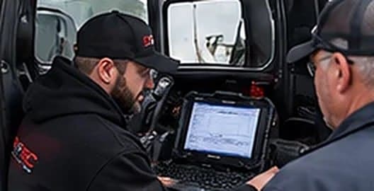 OnTec technician running an initial diagnostic scan on a laptop inside a truck cab with the driver