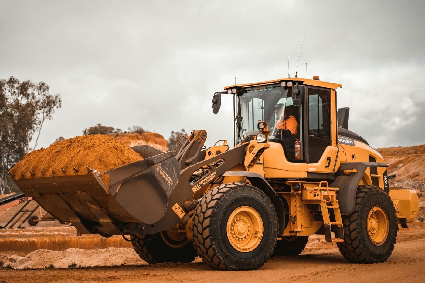 Yellow wheel loader carrying a full bucket of dirt at a work site
