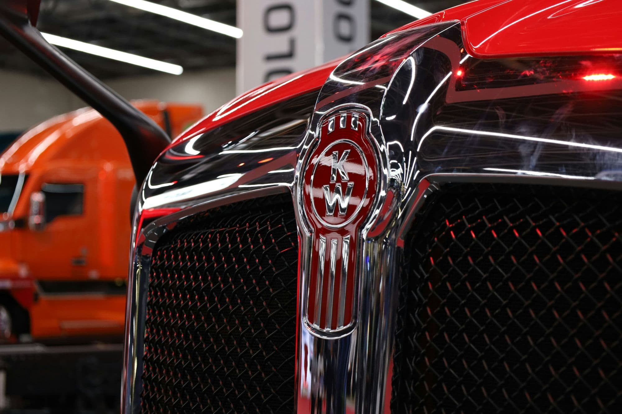 Close-up of a red semi truck hood with a chrome emblem and dark mesh grille