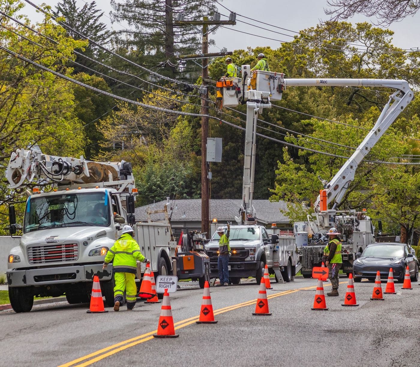 Utility bucket trucks and a service truck with a crew in hi-vis vests working on a street